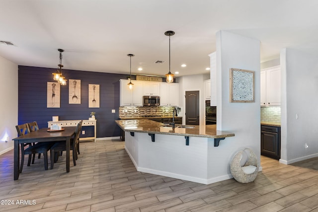 kitchen with sink, hanging light fixtures, dark stone counters, white cabinets, and a breakfast bar area