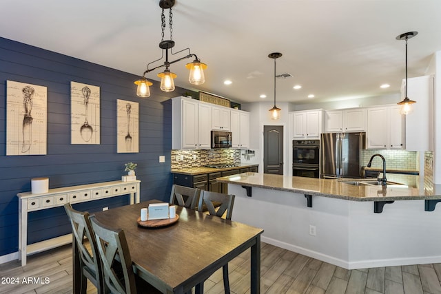 kitchen with wood walls, light hardwood / wood-style floors, stainless steel appliances, decorative light fixtures, and white cabinets