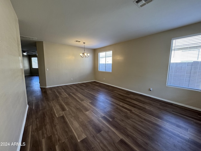 empty room featuring ceiling fan with notable chandelier and dark wood-type flooring