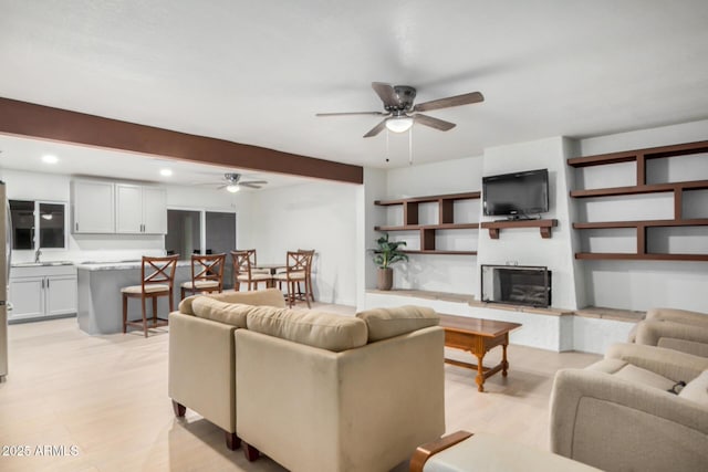 living area with light wood finished floors, a fireplace with raised hearth, beam ceiling, recessed lighting, and a ceiling fan