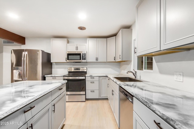 kitchen featuring visible vents, light stone counters, appliances with stainless steel finishes, light wood-style floors, and a sink