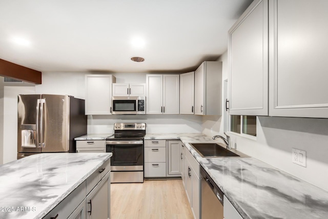 kitchen with light stone counters, light wood-style flooring, appliances with stainless steel finishes, and a sink