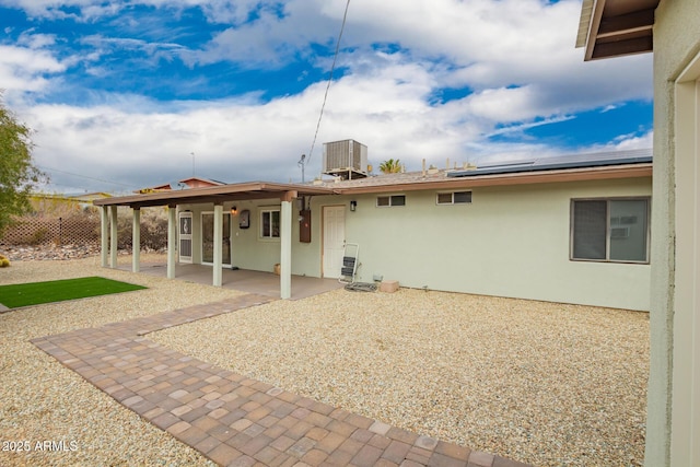 rear view of house with stucco siding, a patio, roof mounted solar panels, and cooling unit