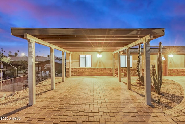 patio terrace at dusk with a carport, decorative driveway, and fence