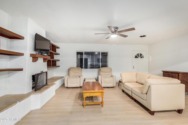 living area featuring a fireplace with raised hearth, light wood-style flooring, and a ceiling fan