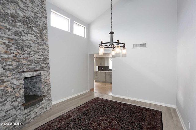 dining space with a chandelier, light hardwood / wood-style floors, high vaulted ceiling, and a stone fireplace