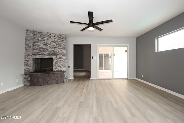 unfurnished living room featuring ceiling fan, a stone fireplace, and light wood-type flooring