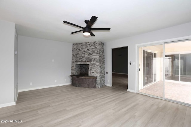 unfurnished living room featuring ceiling fan, a stone fireplace, and light wood-type flooring