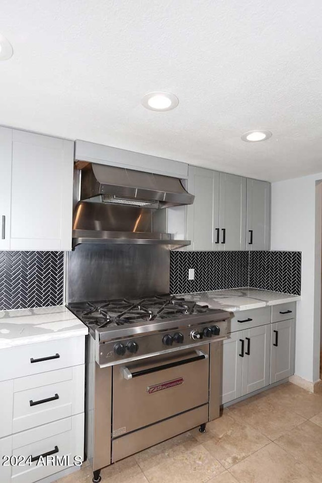 kitchen with backsplash, high end stainless steel range oven, wall chimney exhaust hood, gray cabinets, and light stone counters