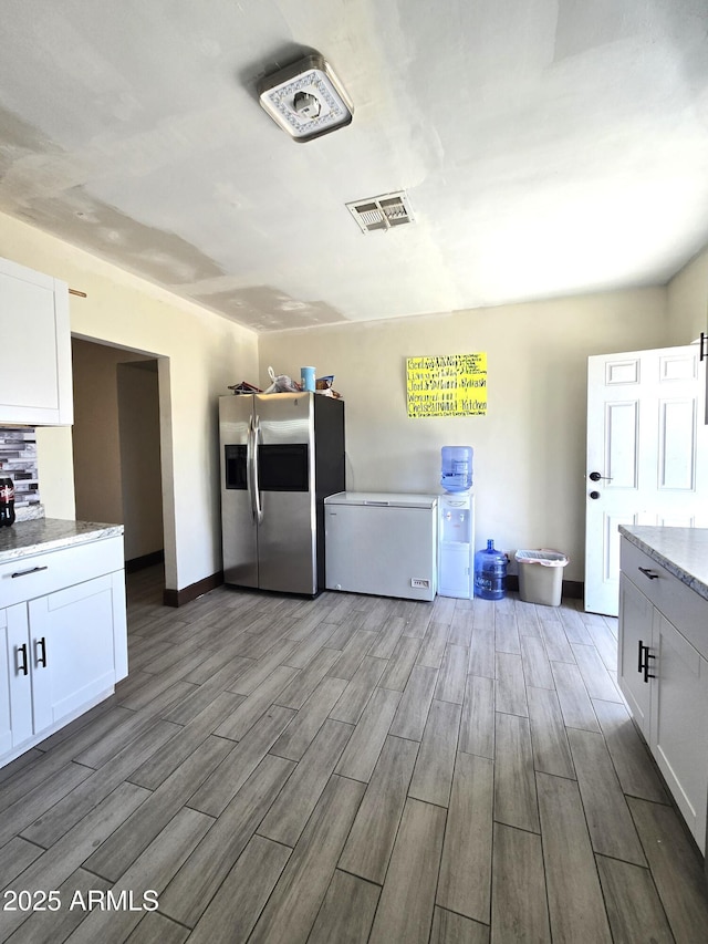 kitchen featuring light stone countertops, stainless steel fridge, visible vents, and white cabinetry