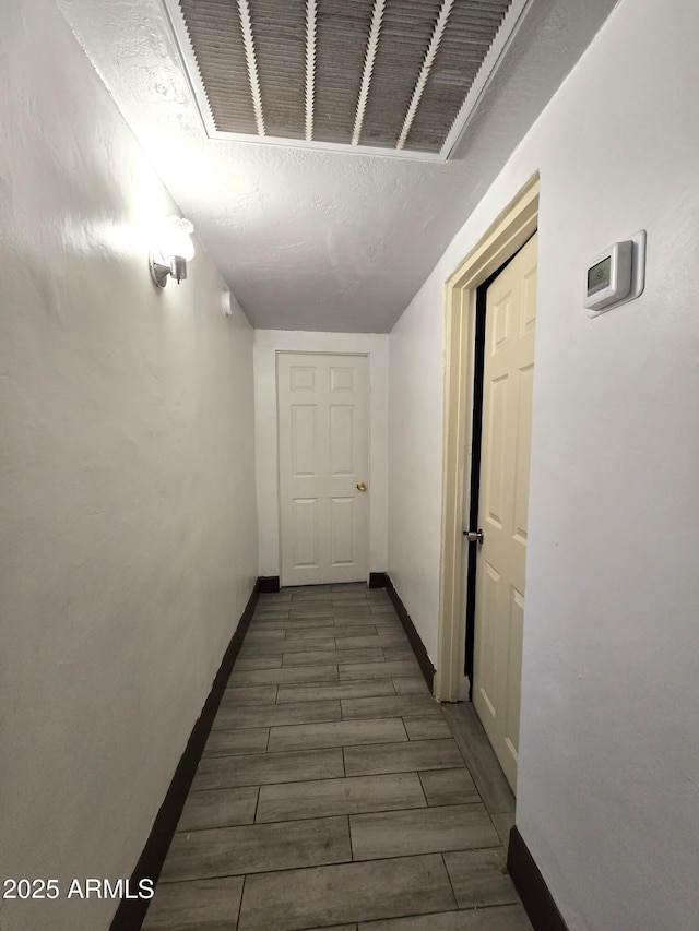 hallway featuring wood tiled floor, visible vents, and baseboards