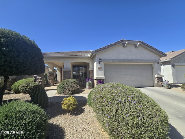 ranch-style house featuring concrete driveway, stone siding, a tiled roof, an attached garage, and stucco siding