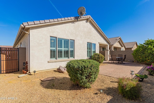 back of house featuring a tiled roof, fence, a patio, and stucco siding