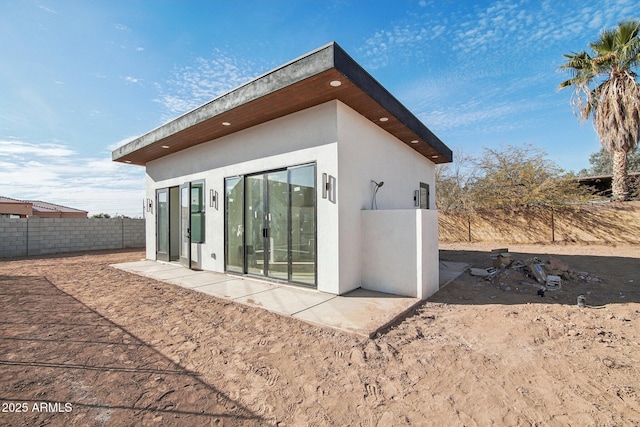 rear view of property featuring fence, stucco siding, and a patio