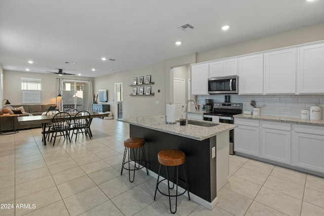 kitchen with a center island with sink, ceiling fan, appliances with stainless steel finishes, light stone counters, and white cabinetry