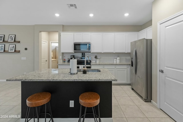 kitchen with stainless steel appliances, light stone counters, an island with sink, a breakfast bar area, and white cabinets