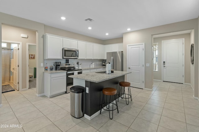 kitchen with backsplash, a breakfast bar, stainless steel appliances, white cabinets, and an island with sink