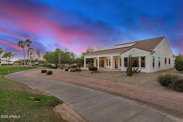 back house at dusk featuring covered porch and solar panels