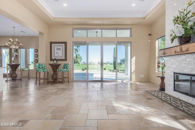 interior space featuring a stone fireplace, plenty of natural light, a chandelier, and a high ceiling