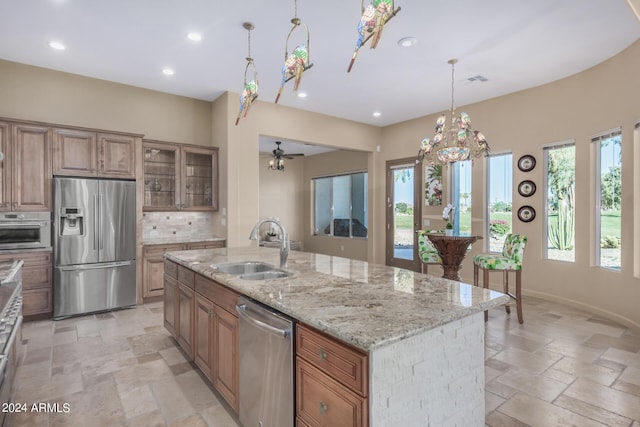 kitchen with a center island with sink, sink, light stone countertops, decorative light fixtures, and stainless steel appliances