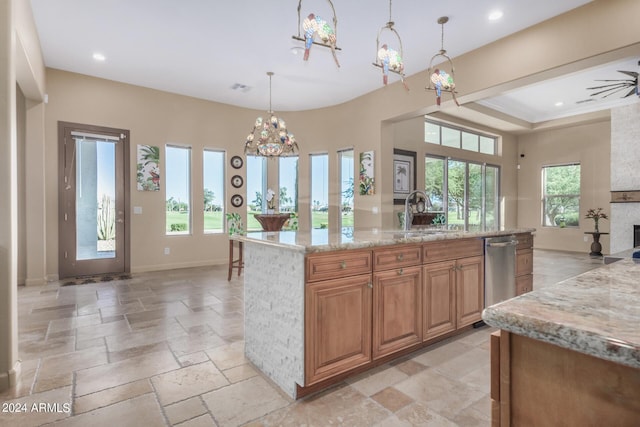 kitchen with a large fireplace, sink, light stone counters, an island with sink, and pendant lighting