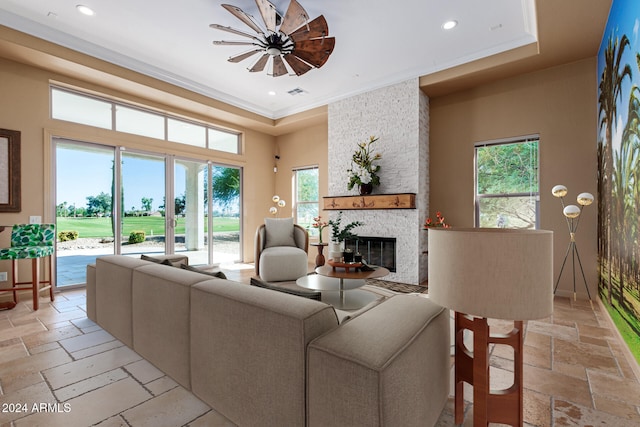 living room featuring ceiling fan, a stone fireplace, and ornamental molding