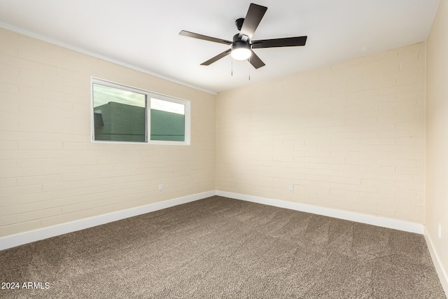 carpeted spare room featuring ceiling fan and brick wall