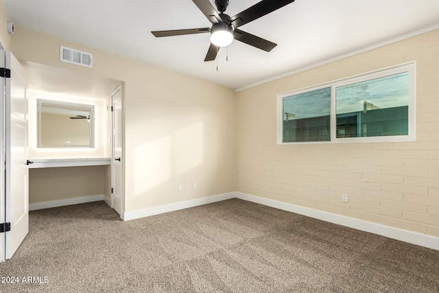 carpeted empty room with ceiling fan and brick wall