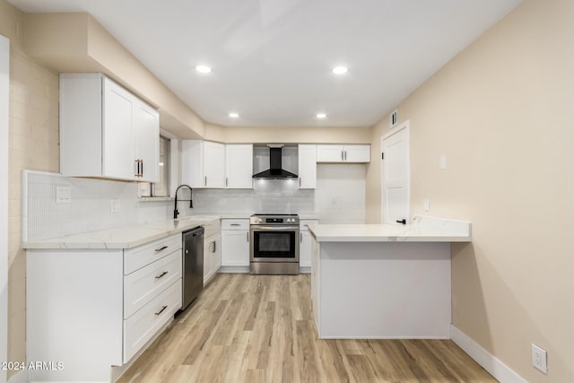 kitchen with appliances with stainless steel finishes, light wood-type flooring, wall chimney exhaust hood, sink, and white cabinets