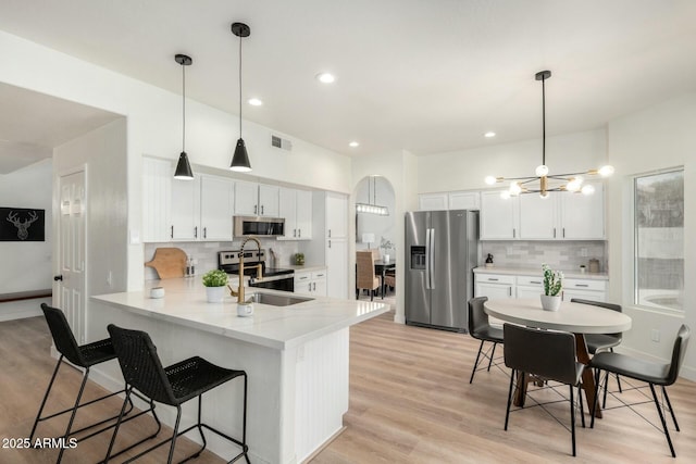 kitchen with stainless steel appliances, white cabinetry, hanging light fixtures, and kitchen peninsula