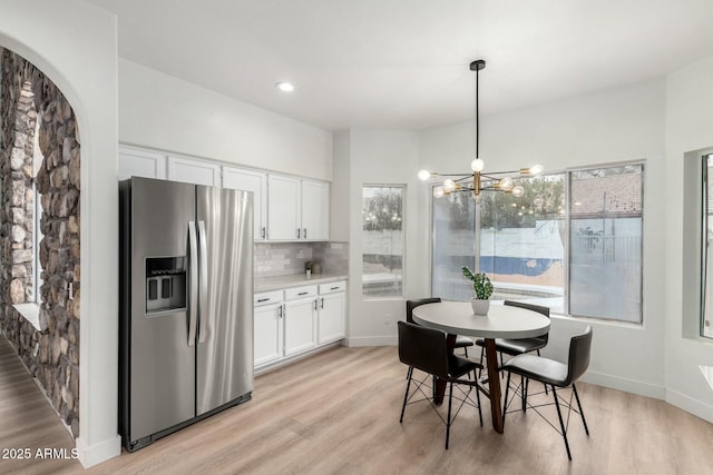 kitchen featuring stainless steel refrigerator with ice dispenser, tasteful backsplash, light hardwood / wood-style flooring, hanging light fixtures, and white cabinets