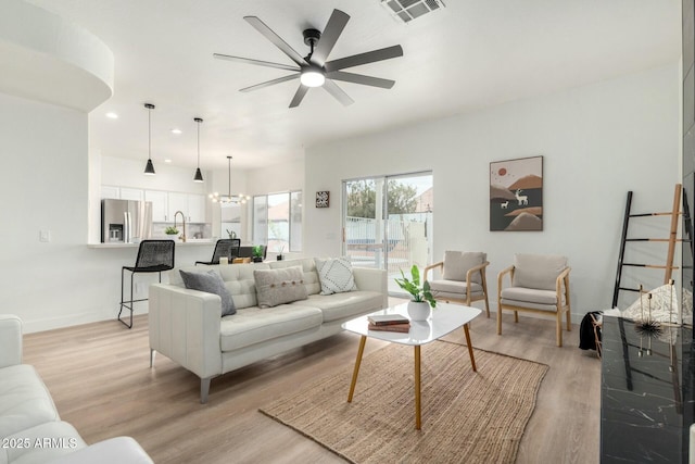 living room with sink, ceiling fan with notable chandelier, and light hardwood / wood-style flooring