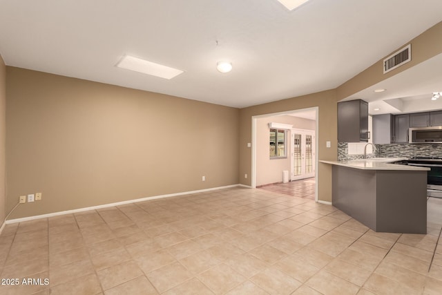 kitchen with kitchen peninsula, tasteful backsplash, stainless steel appliances, sink, and light tile patterned flooring