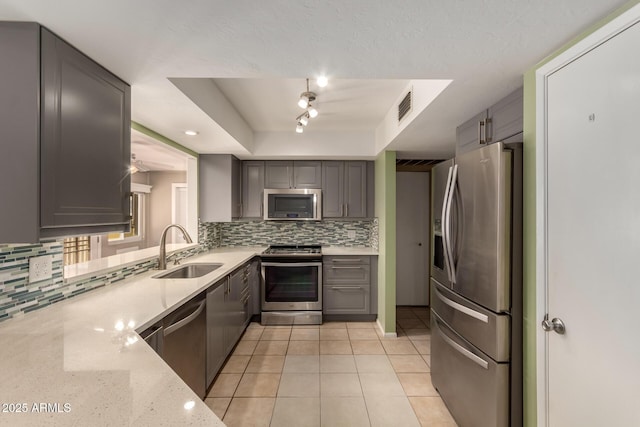 kitchen featuring sink, gray cabinets, light stone countertops, appliances with stainless steel finishes, and a tray ceiling