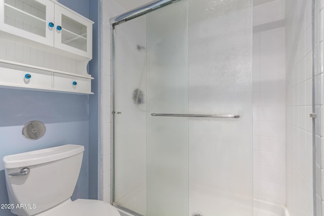 bathroom featuring a shower with door and toilet