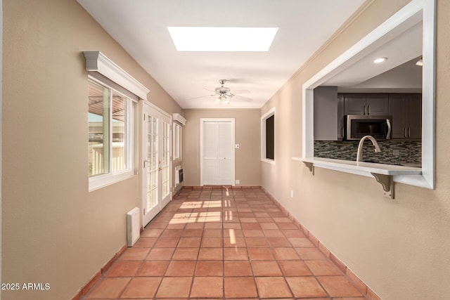 corridor featuring a skylight, crown molding, and light tile patterned floors