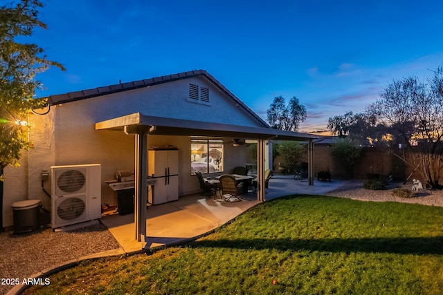 back house at dusk featuring a patio area and a lawn