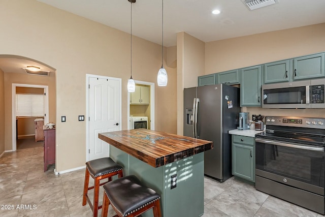 kitchen featuring appliances with stainless steel finishes, decorative light fixtures, washer / clothes dryer, wooden counters, and a kitchen breakfast bar