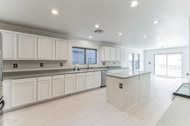 kitchen featuring white cabinets, stainless steel dishwasher, a kitchen island, and sink