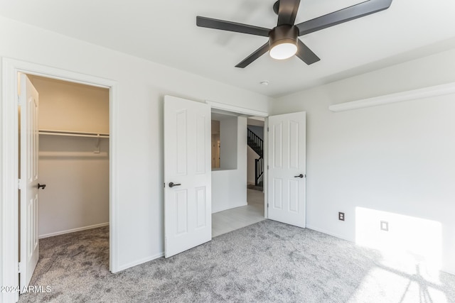 unfurnished bedroom with a walk in closet, ceiling fan, a closet, and light colored carpet