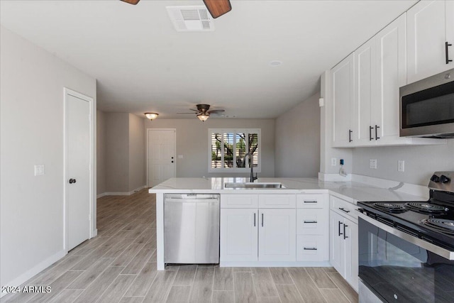 kitchen with appliances with stainless steel finishes, white cabinets, kitchen peninsula, light hardwood / wood-style flooring, and sink