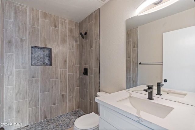 bathroom featuring a tile shower, vanity, and toilet