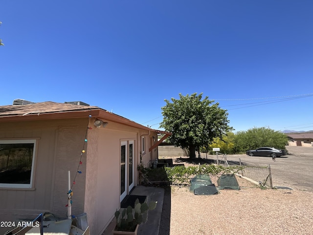 view of home's exterior with a shingled roof, fence, and stucco siding