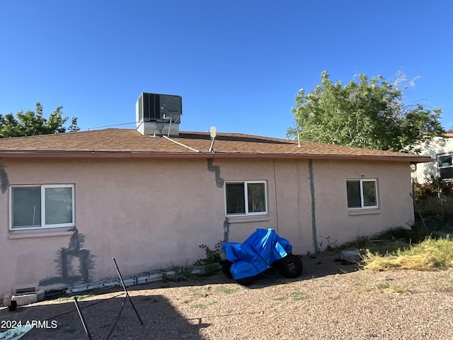 back of house featuring a shingled roof, stucco siding, and central air condition unit