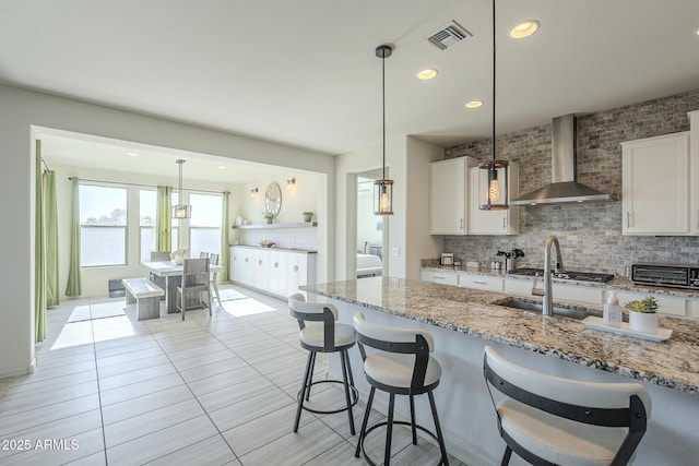 kitchen featuring white cabinetry, decorative backsplash, hanging light fixtures, light stone countertops, and wall chimney range hood