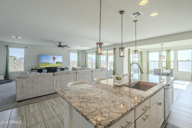 kitchen featuring pendant lighting, white cabinetry, sink, light stone counters, and a center island with sink