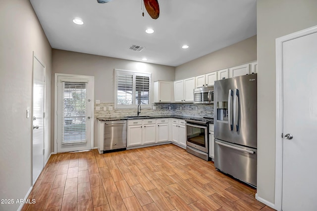 kitchen featuring appliances with stainless steel finishes, sink, white cabinets, decorative backsplash, and ceiling fan