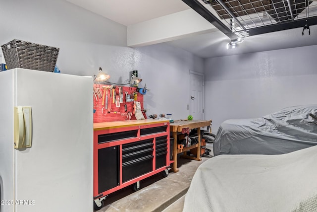 bedroom featuring a workshop area, white fridge, and concrete floors