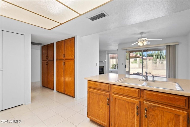 kitchen with light tile patterned floors, ceiling fan, a textured ceiling, a brick fireplace, and sink