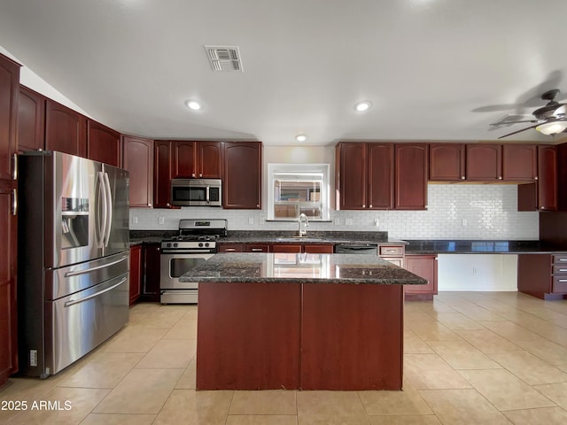 kitchen with sink, stainless steel appliances, dark stone counters, and a kitchen island